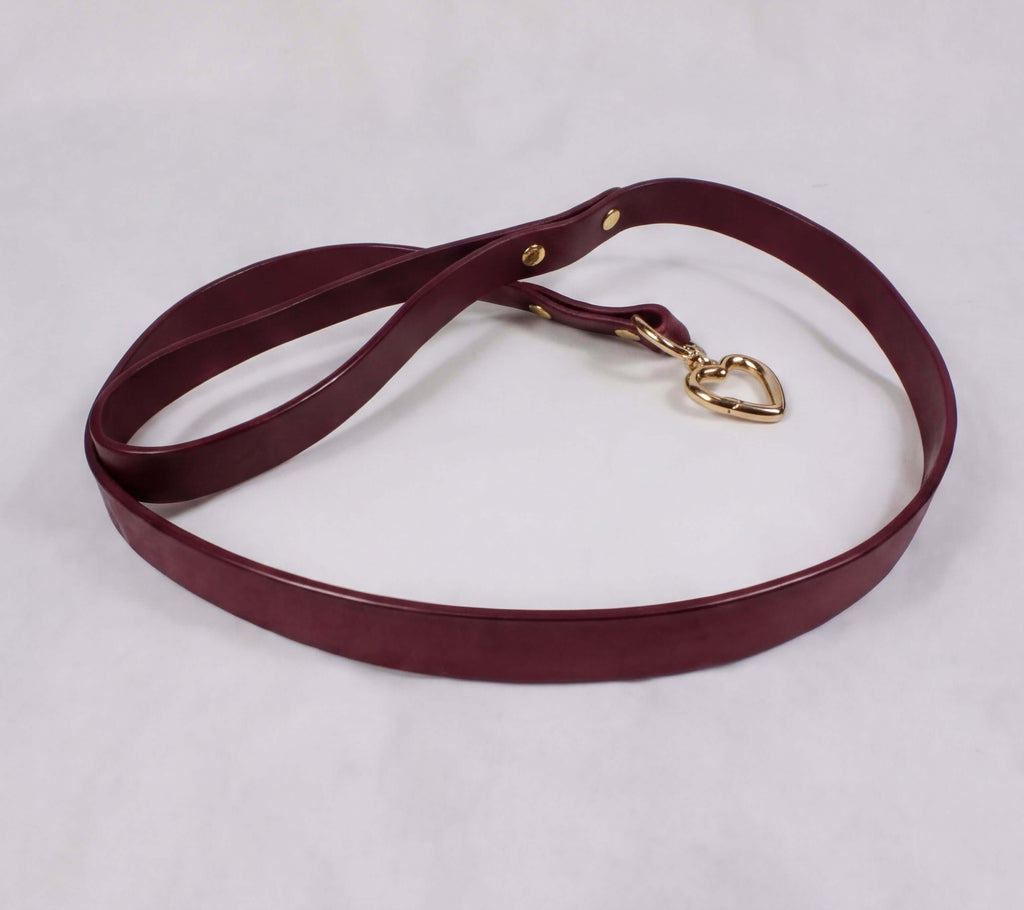 A burgundy leather dog leash with a gold heart-shaped charm attached.