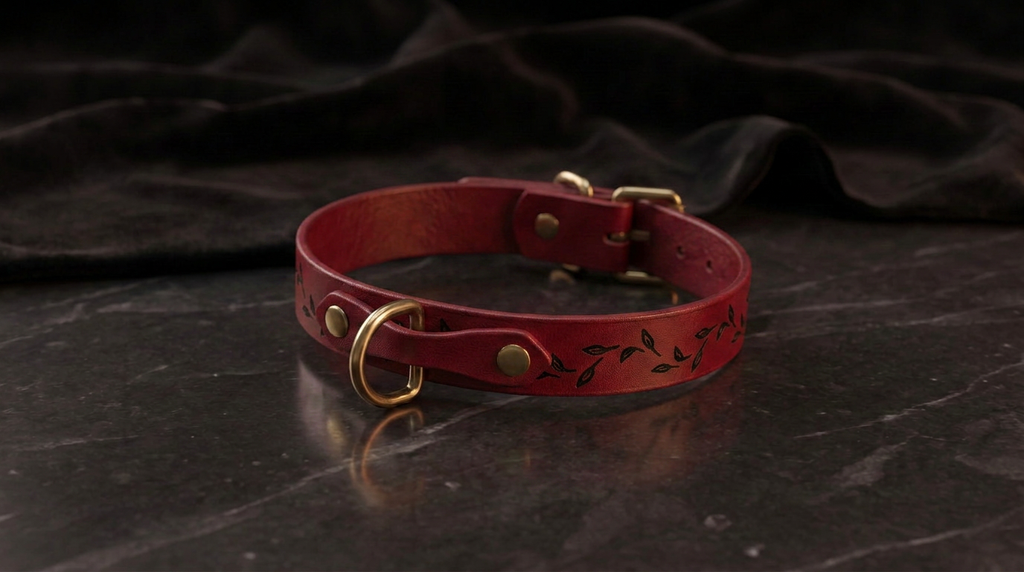 A red leather collar with a leaf design sits on a dark surface.