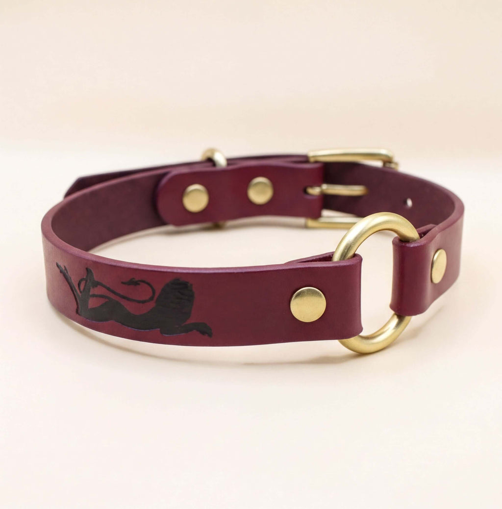 A burgundy leather dog collar with a gold buckle and a black lion silhouette on the front.