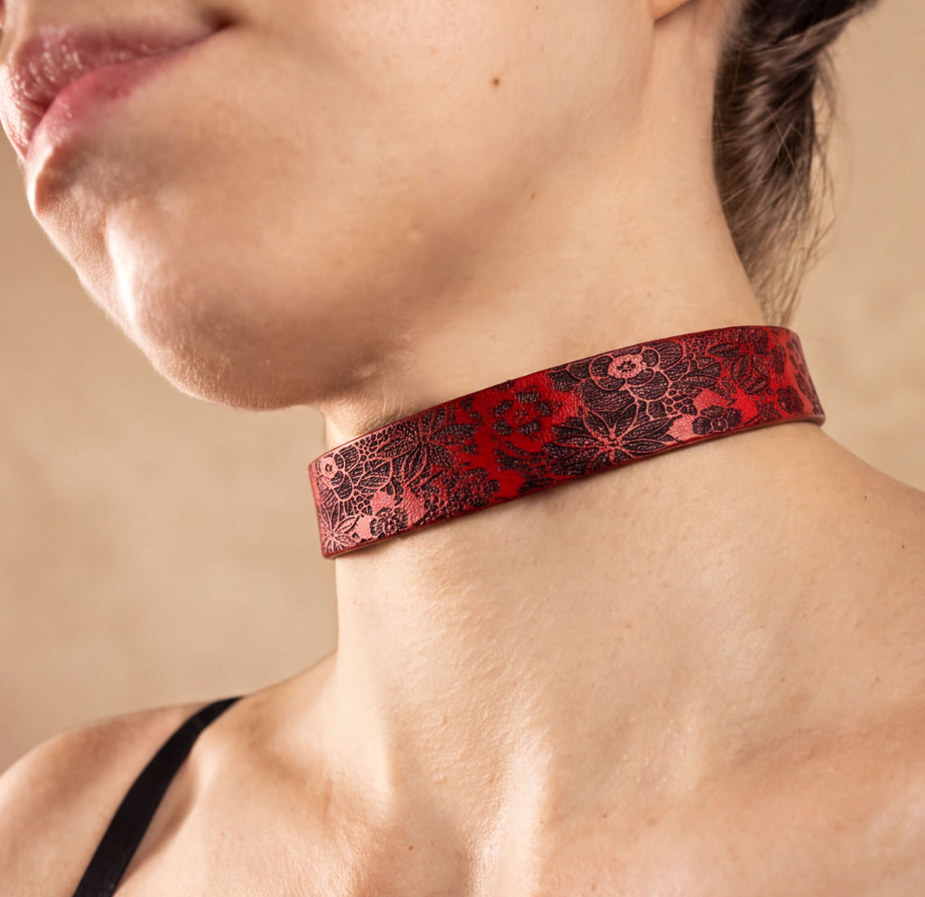 A close-up of a woman's neck and chest area wearing a red choker necklace with a floral pattern.