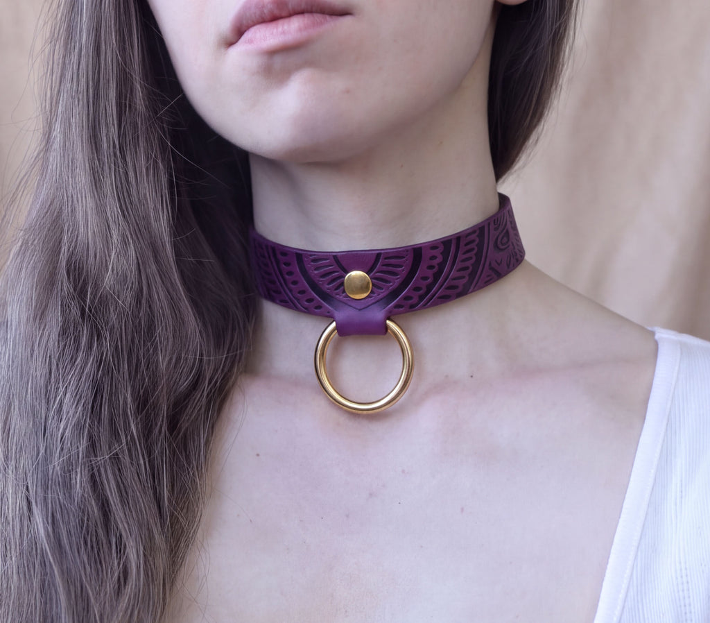 A close-up of a woman's neck and chest area wearing a purple choker necklace with a gold ring.