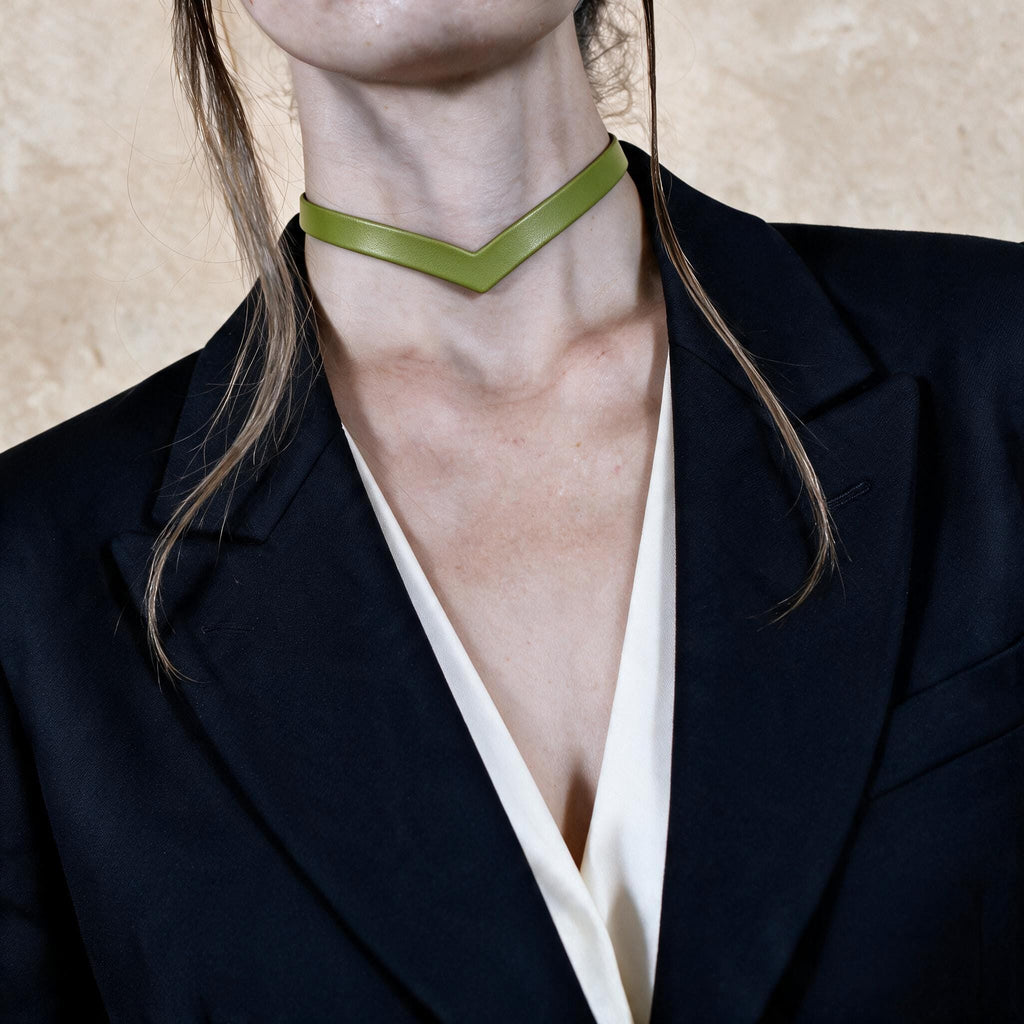 A close-up of a person wearing a black blazer and a green choker necklace.