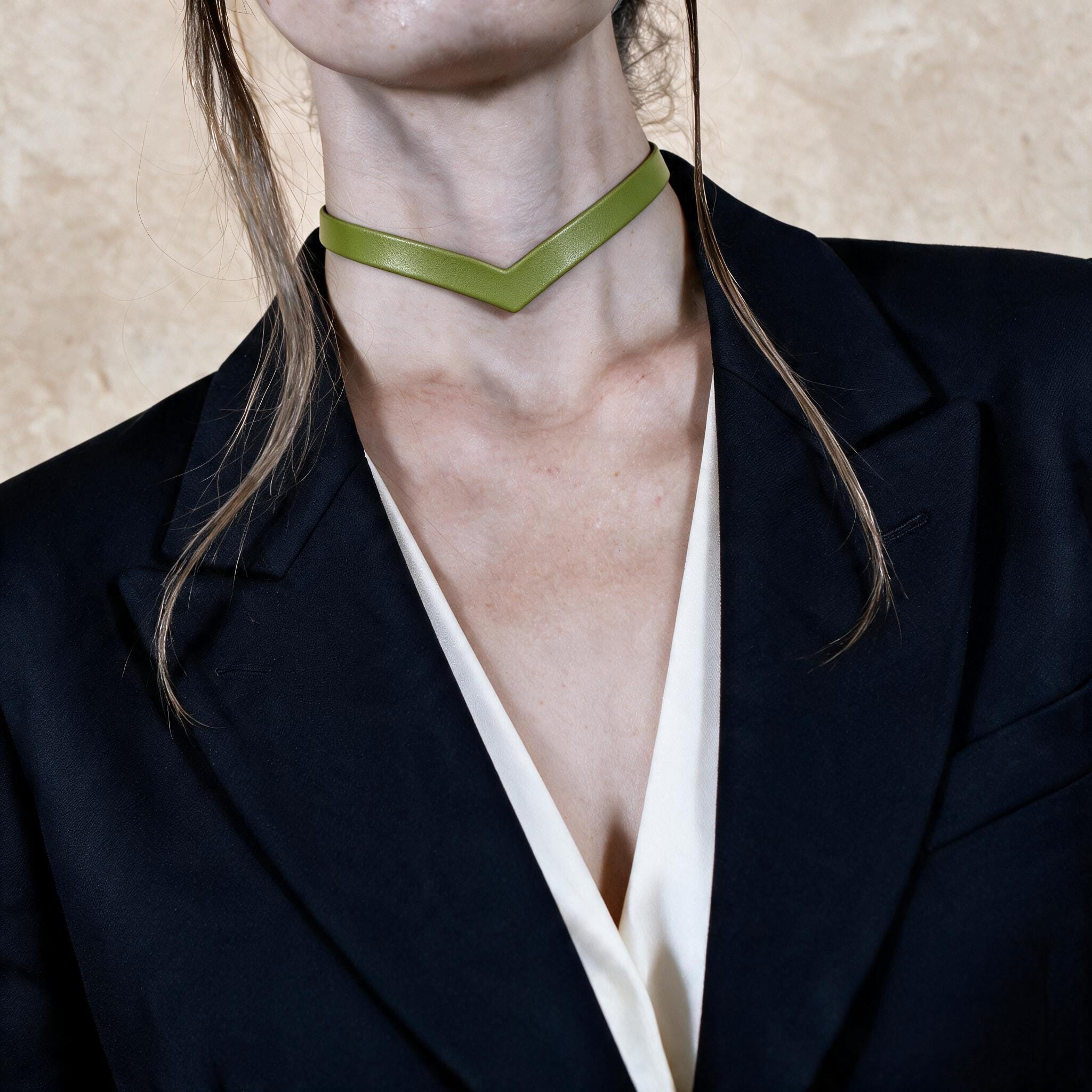 A close-up of a person wearing a black blazer and a green choker necklace.