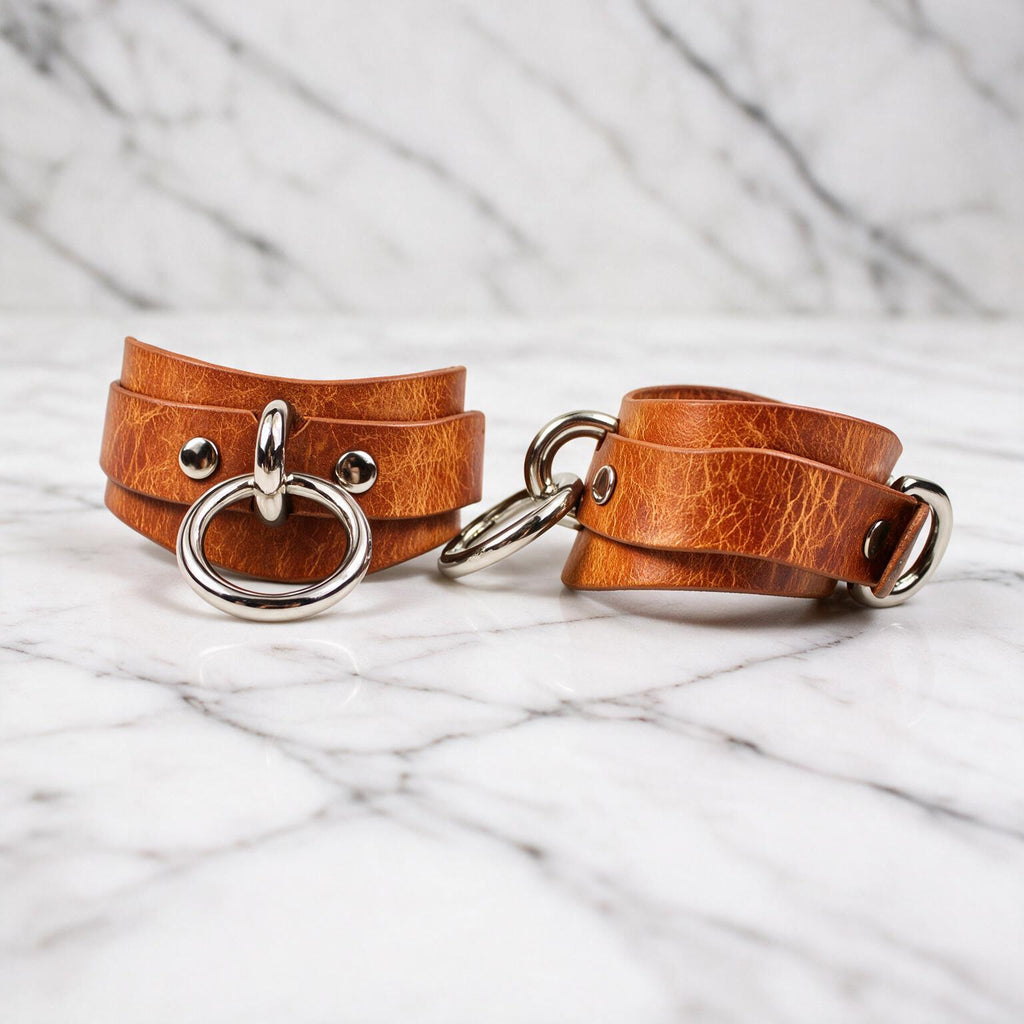 Two leather straps with metal rings and buckles are placed on a marble surface.