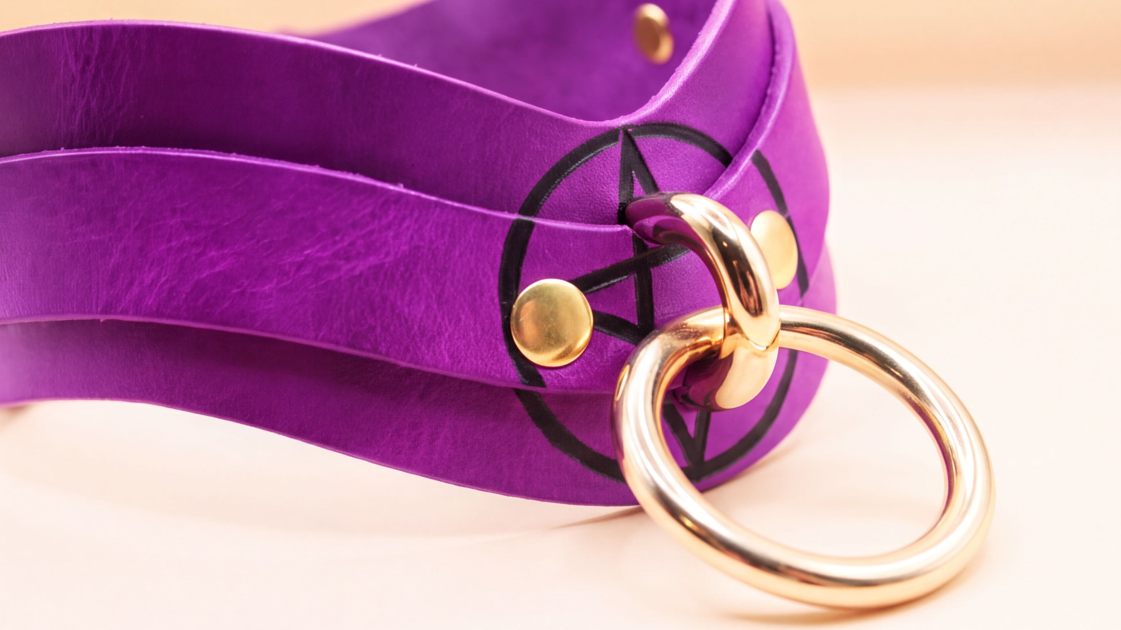 A purple leather choker necklace with a gold ring and a black symbol on it.