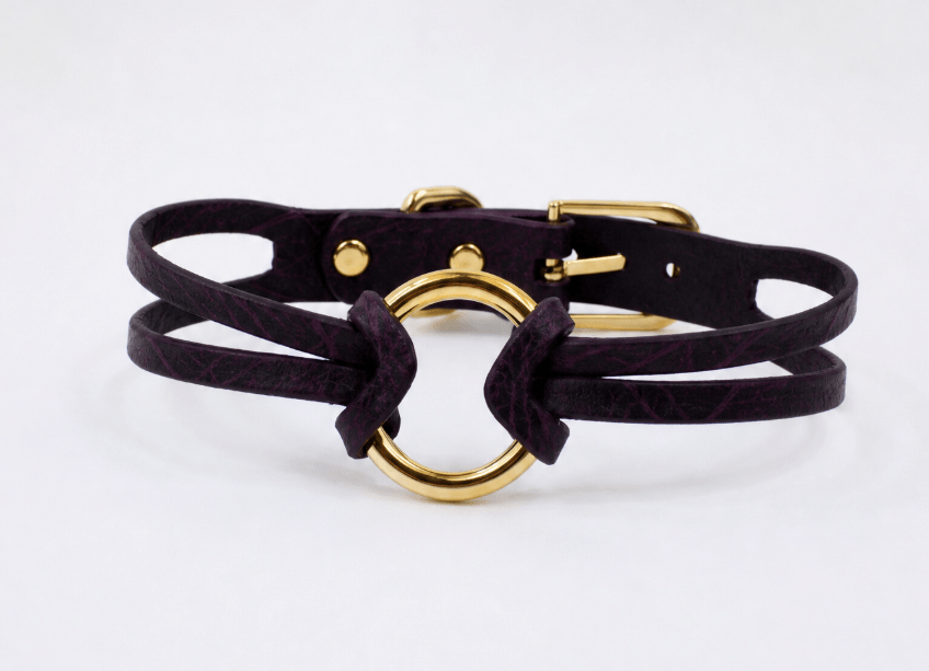 A purple leather choker necklace with a gold-colored circular buckle.