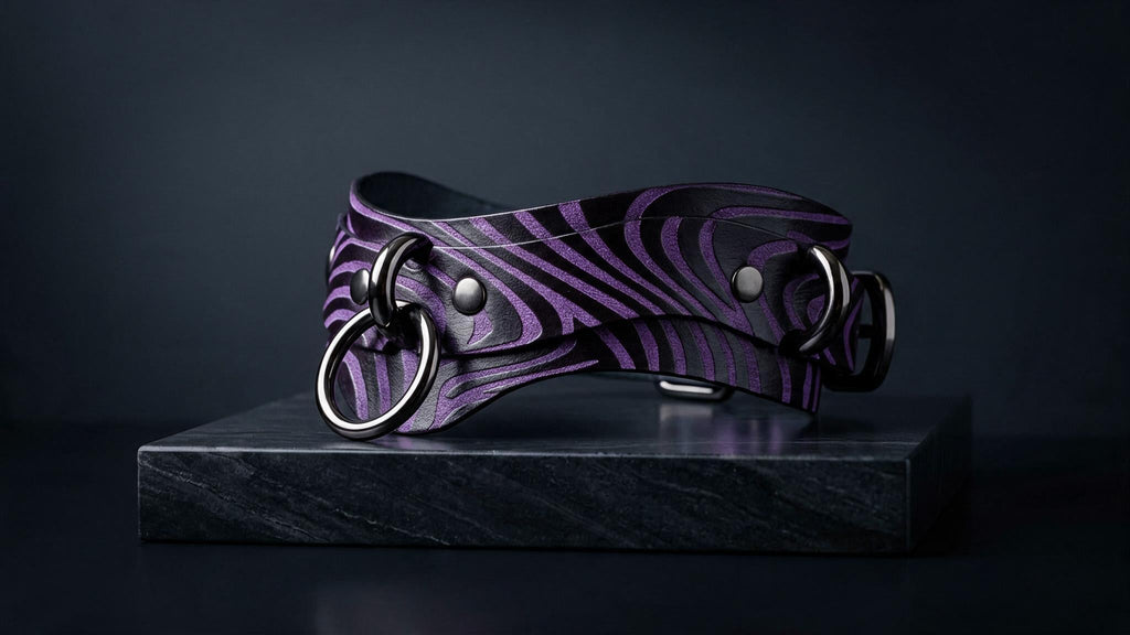 A purple zebra-striped leather collar with metal rings and buckles is displayed on a black marble pedestal against a dark background.
