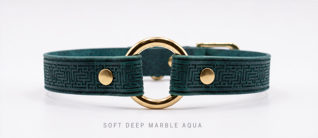 A close-up image of a green leather collar with a gold-colored metal ring and two gold-colored metal buttons.