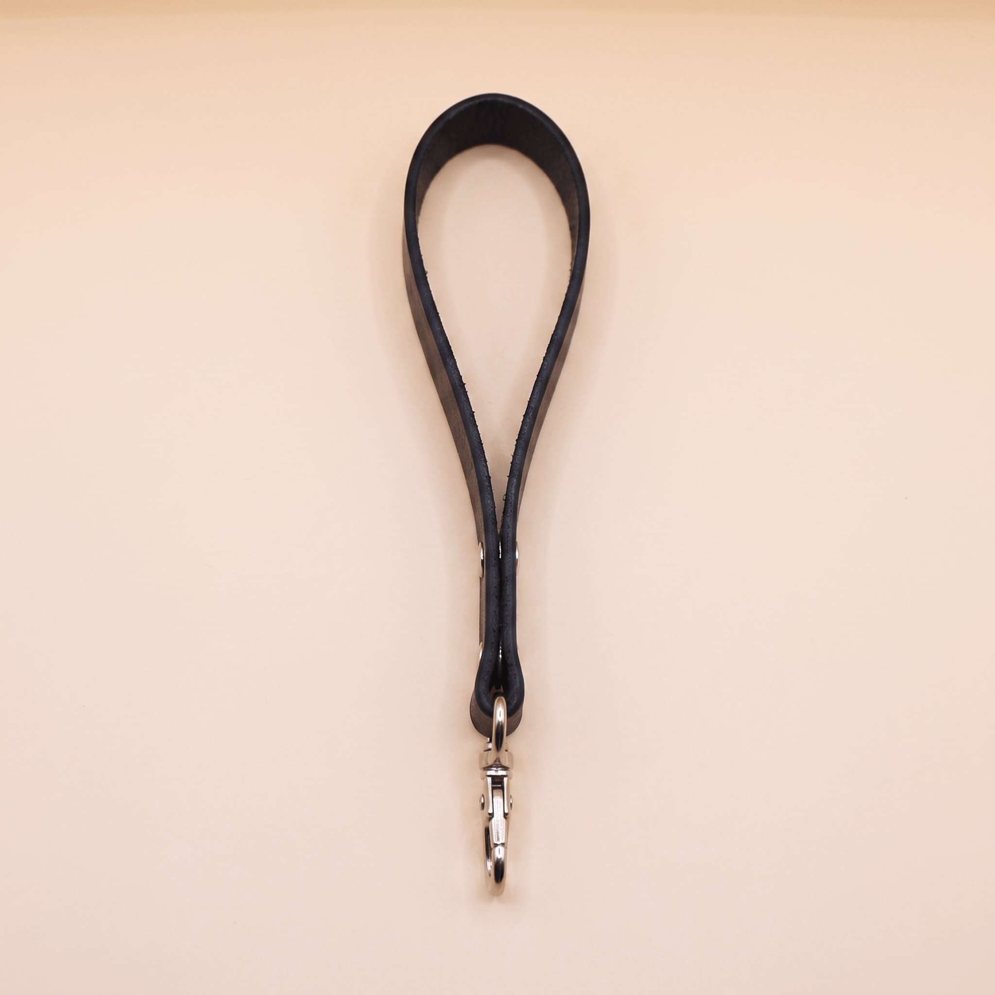 A black leather strap with a metal clasp attached to it, hanging against a light-colored background.