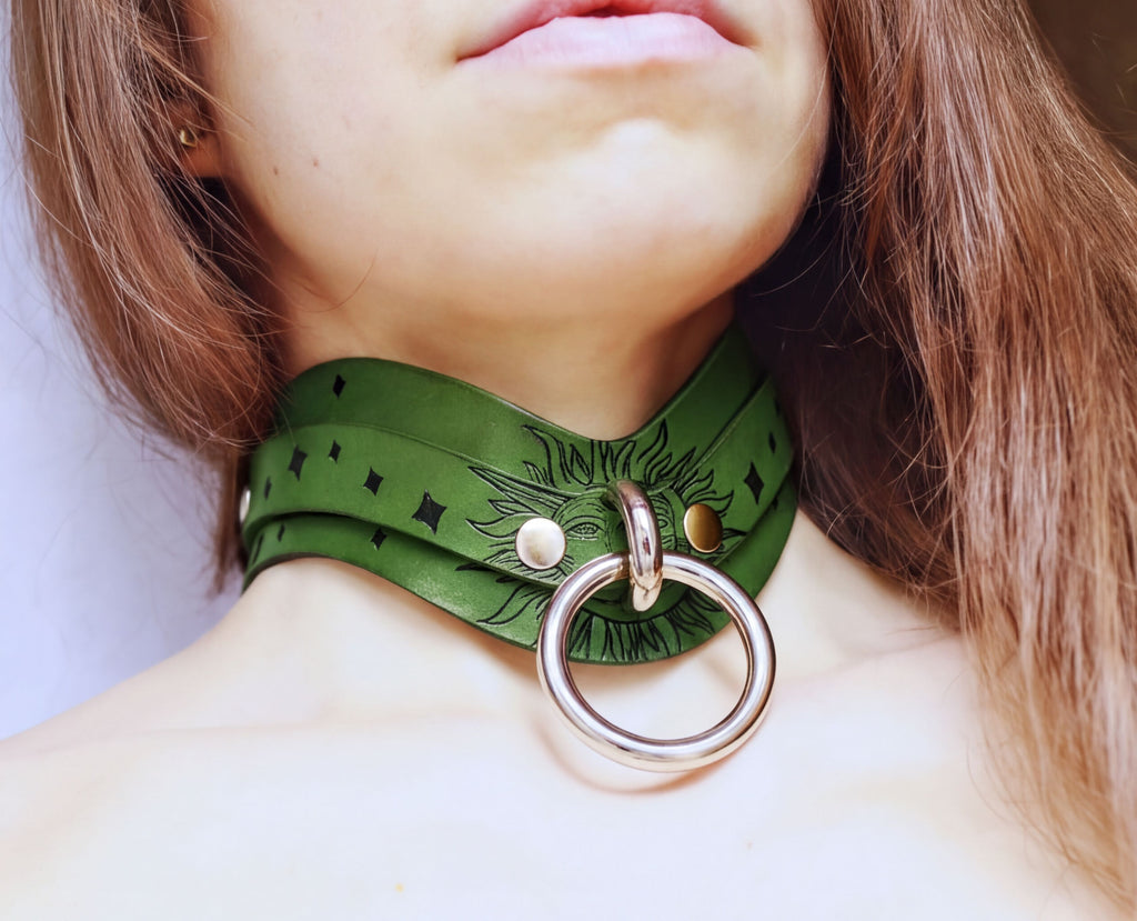 A close-up of a woman's neck and chest area, featuring a green choker necklace with a metal ring and a decorative design.