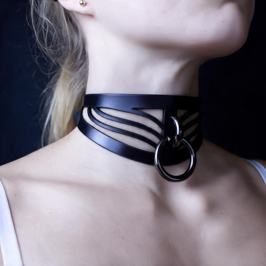 A close-up of a woman's neck and chest area wearing a black choker necklace with a metal ring.