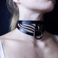 A close-up of a woman's neck and chest area wearing a black choker necklace with a metal ring.