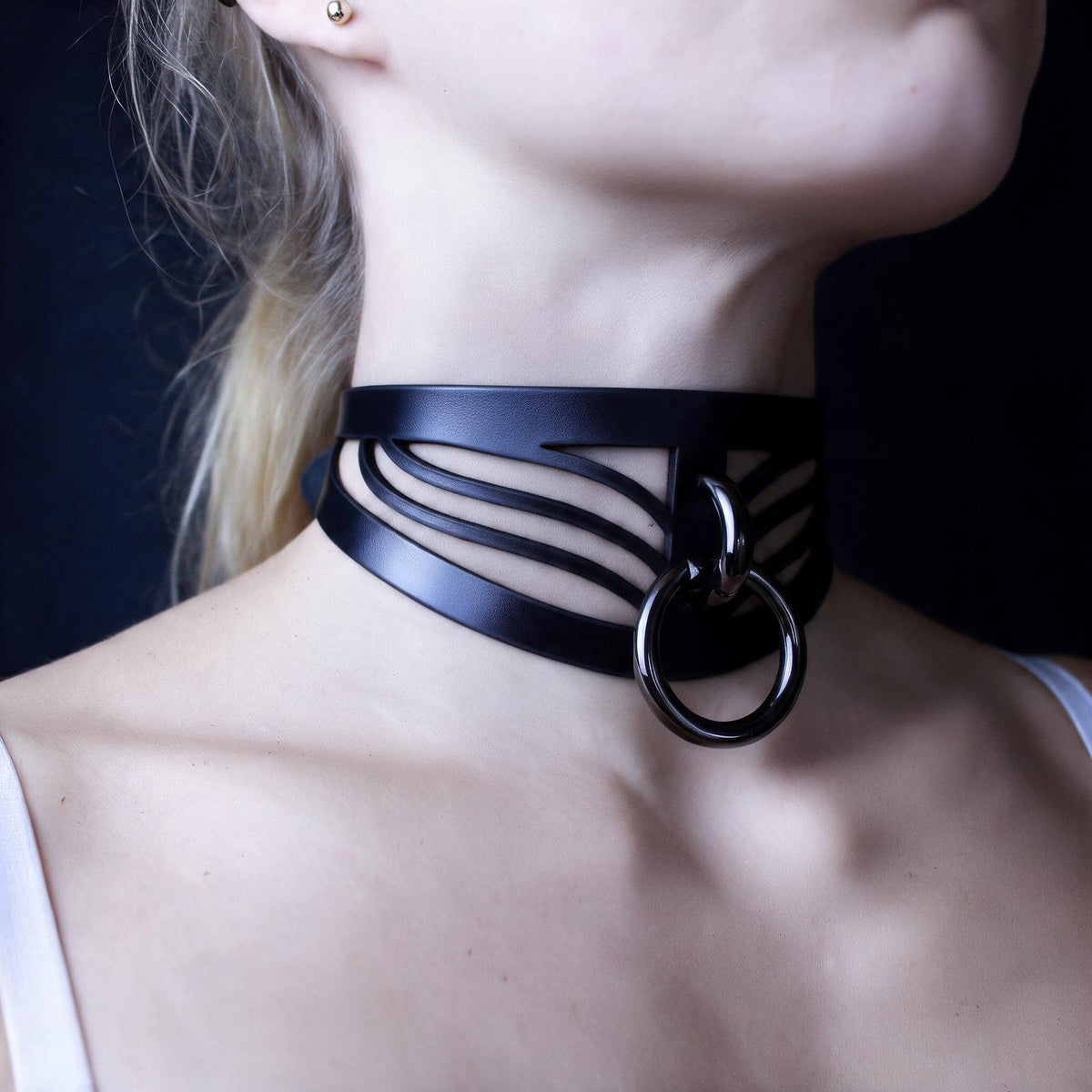 A close-up of a woman's neck and chest area wearing a black choker necklace with a metal ring.