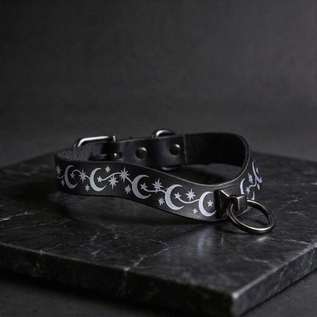 A black leather collar with a silver metal ring and a star and crescent design on it, resting on a dark surface.