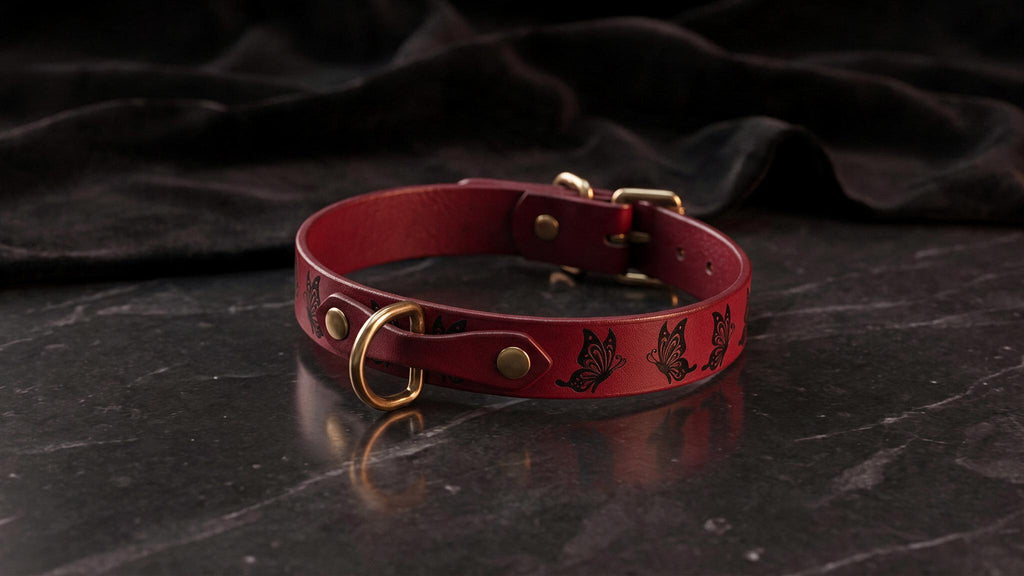 A red leather collar with gold hardware and butterfly designs is displayed on a dark surface.