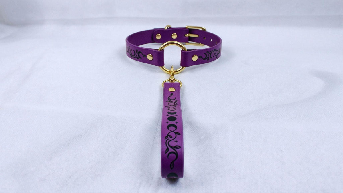 A purple leather collar with a gold-colored buckle and a black and white patterned strap.