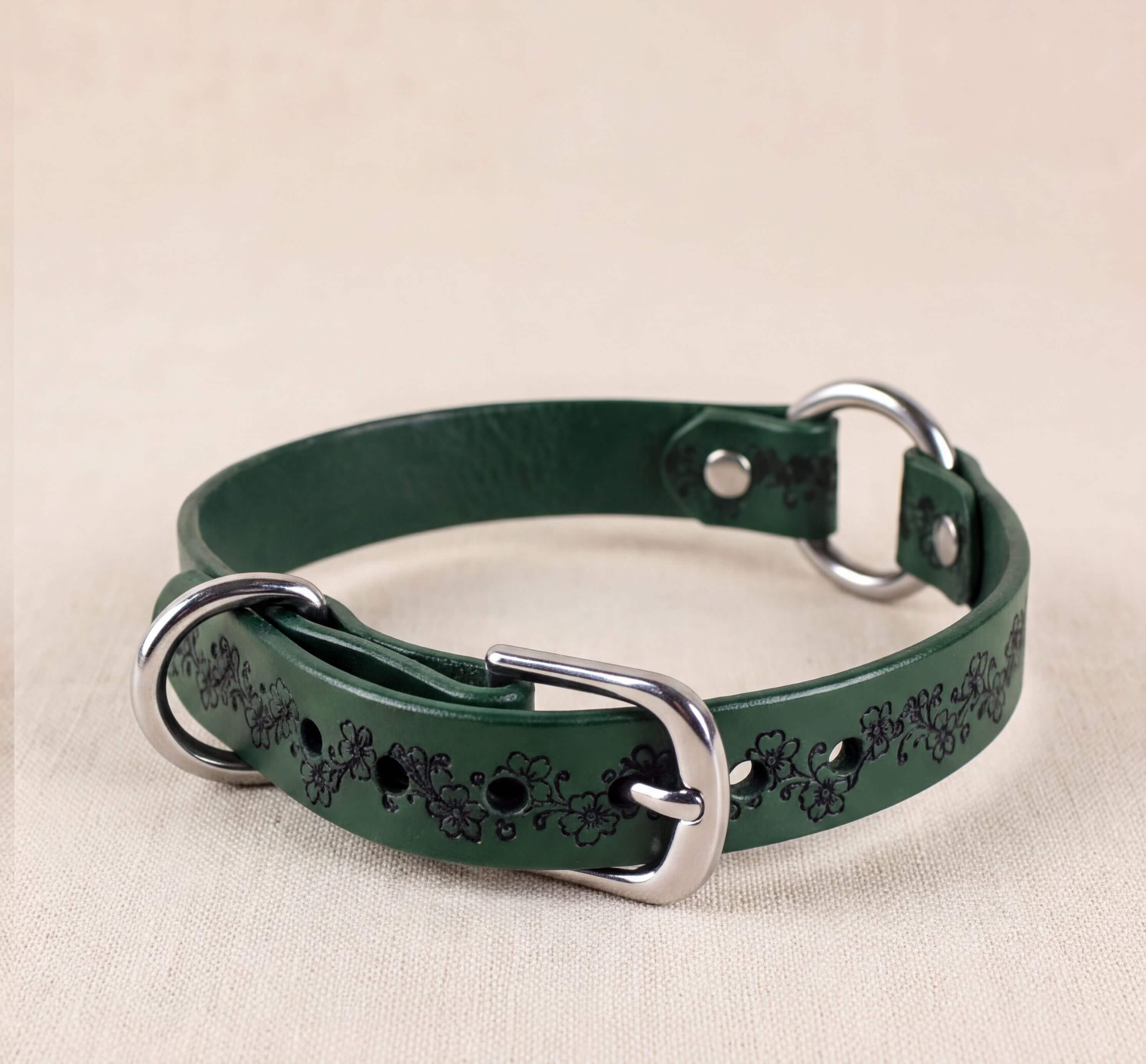 A green leather dog collar with a floral pattern and metal rings.