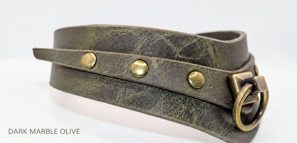 A close-up view of a dark green leather choker necklace with brass hardware, including three round buttons and a ring-like clasp.