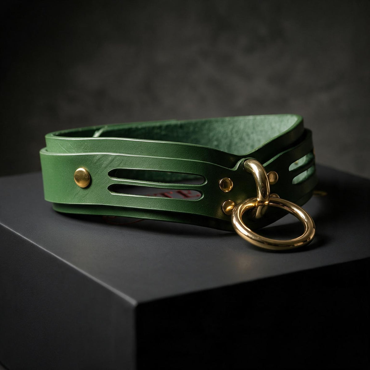 A green leather choker necklace with a gold ring and buckle is displayed on a black surface.