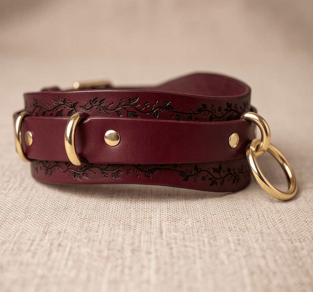 A burgundy leather strap with gold rings and a floral design on the surface.