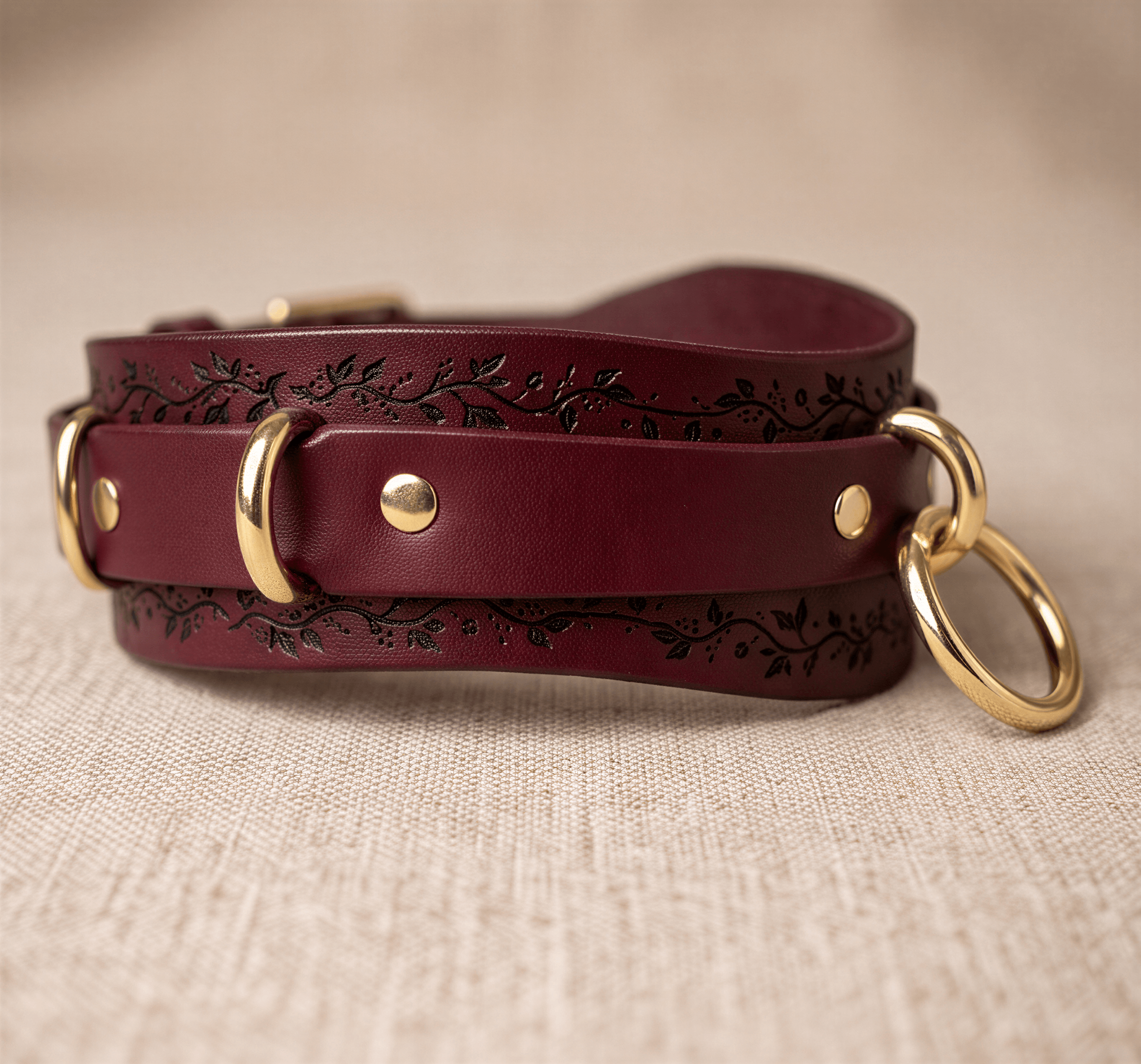 A burgundy leather strap with gold rings and a floral design on the surface.