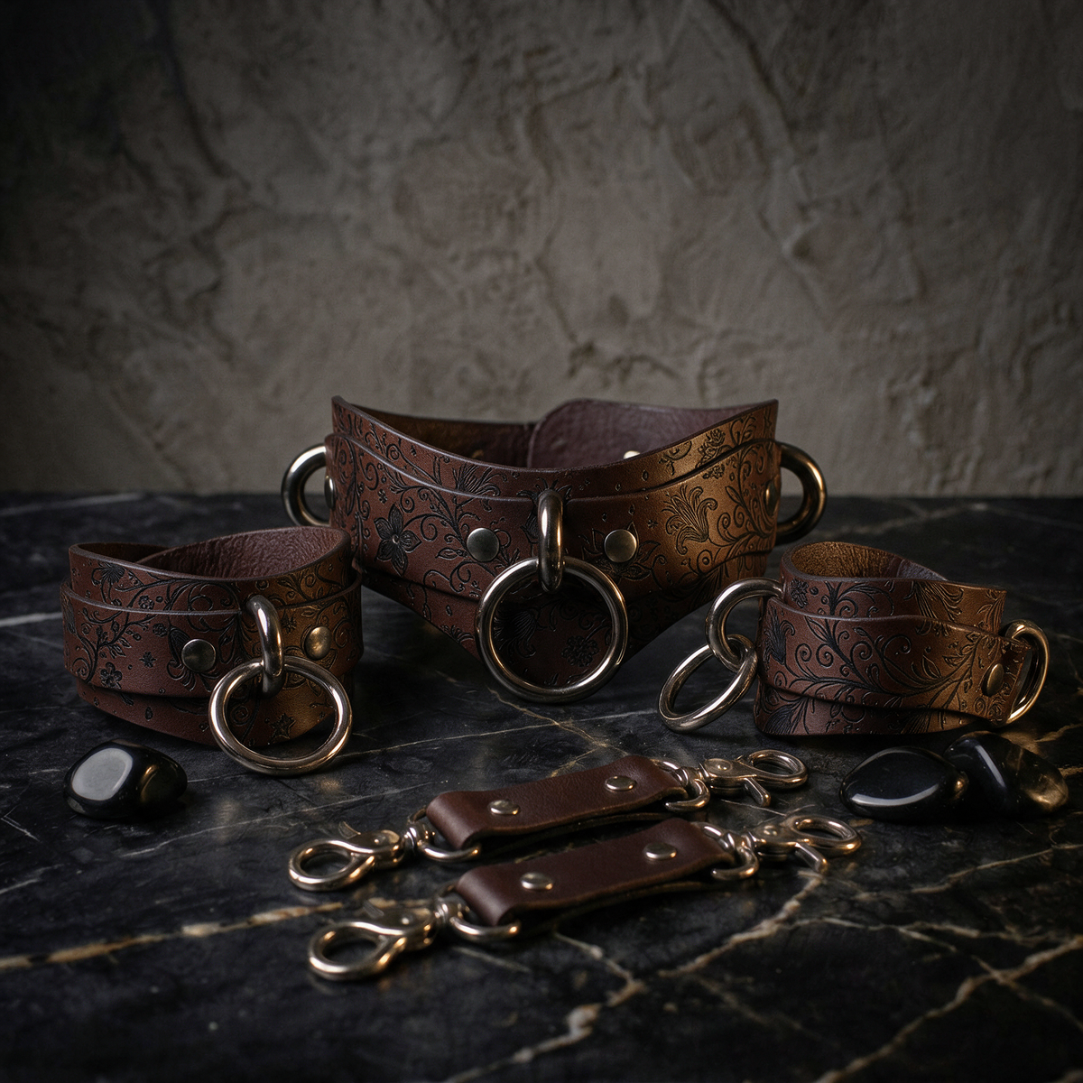 A set of brown leather straps with metal rings and buckles, arranged on a dark surface.