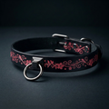 A black leather collar with a floral design and a metal ring on the front.