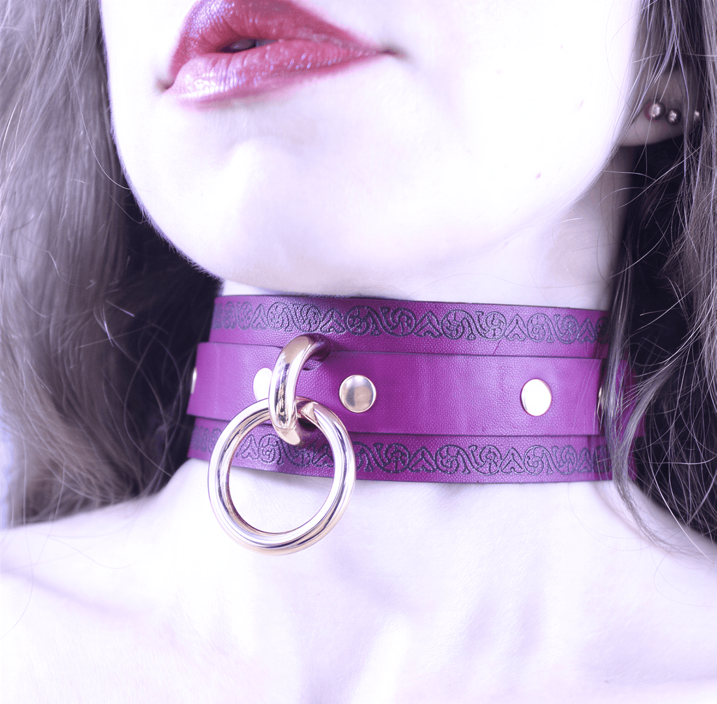 A close-up of a woman's neck and chin wearing a purple choker necklace with a gold ring.