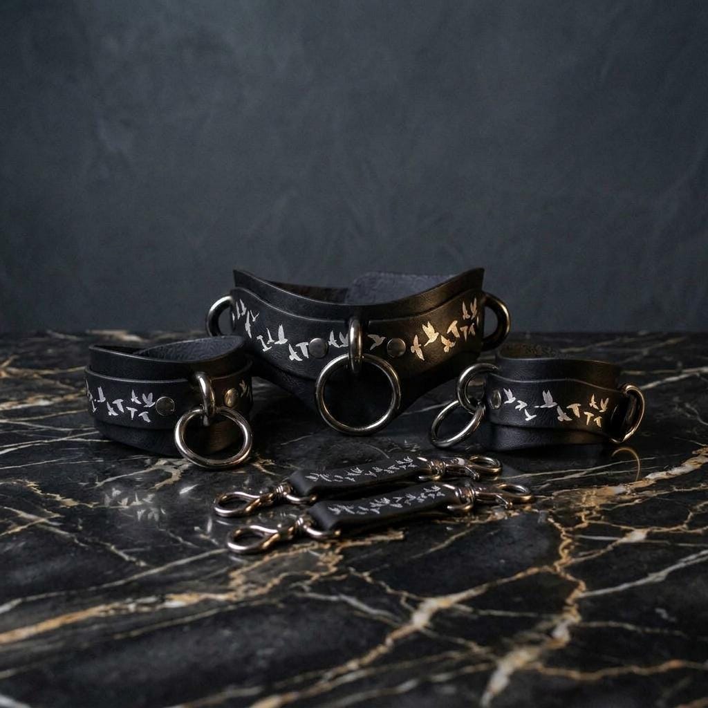 A set of black leather choker necklaces with silver rings and handles, arranged on a marble surface.