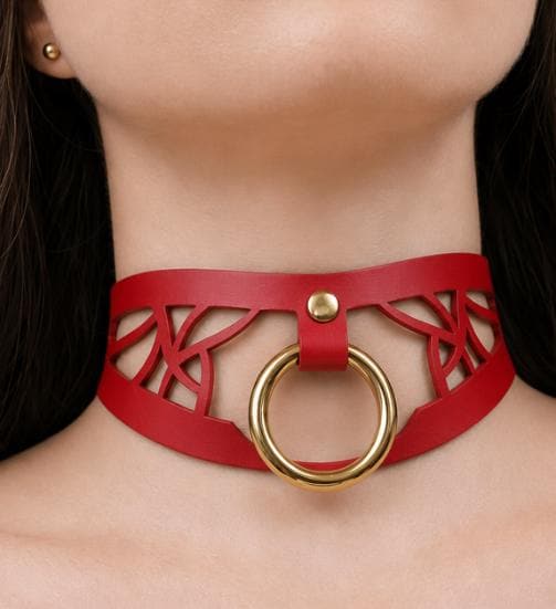 A close-up of a woman's neck wearing a red choker necklace with a gold ring.