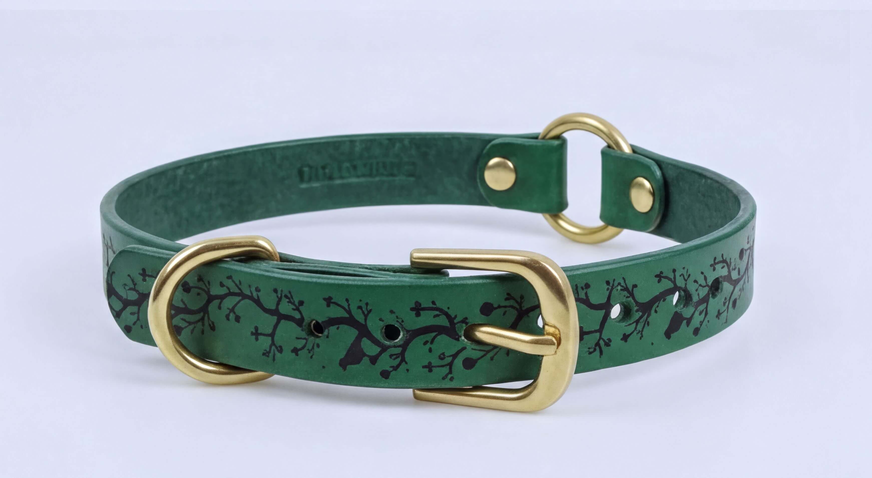 A green leather dog collar with a gold buckle and a tree branch pattern.