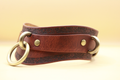 A brown leather strap with metal rings and buckles, resting on a plain background.
