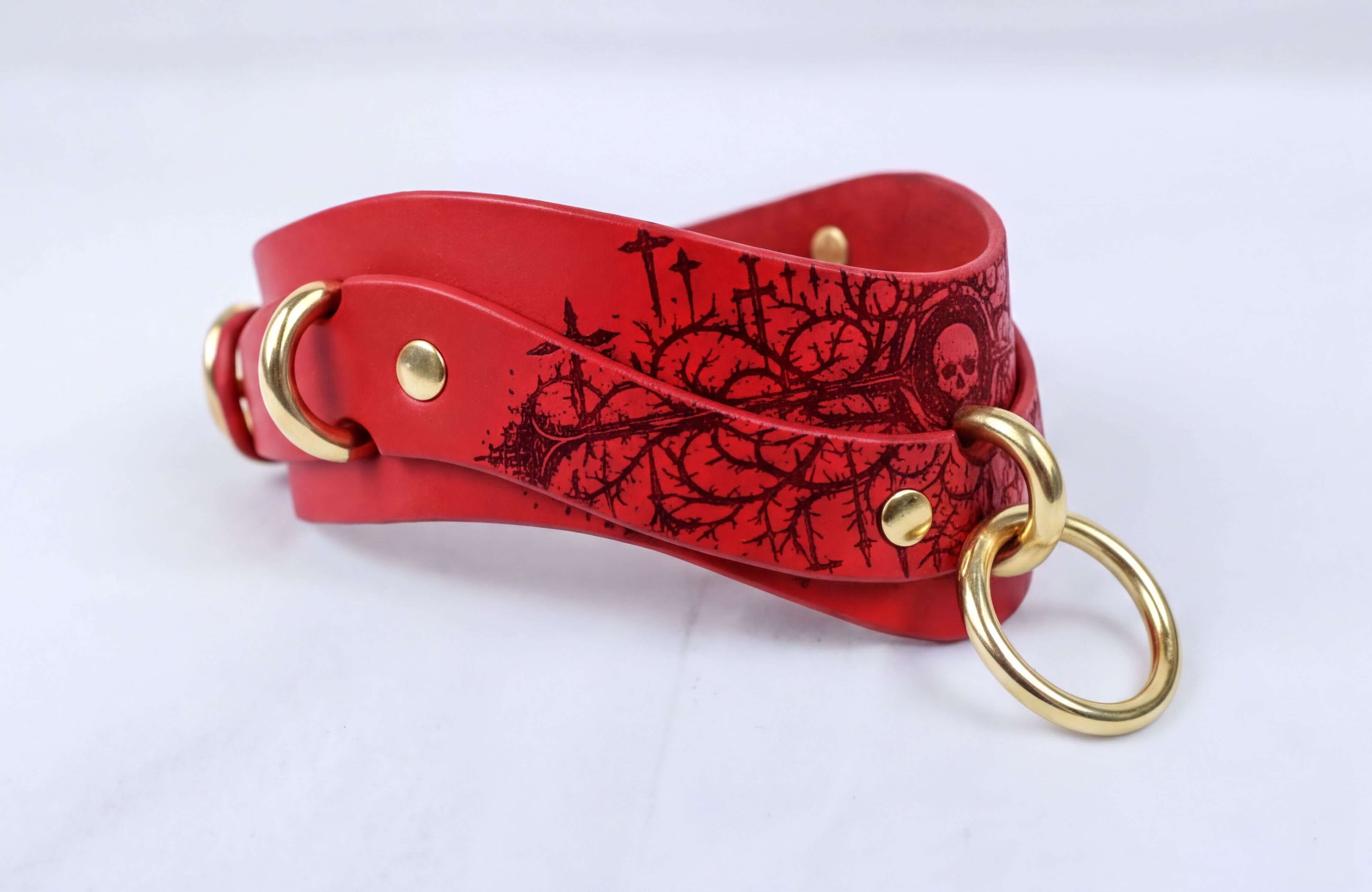 A red leather choker necklace with a black floral design and gold-colored metal rings.