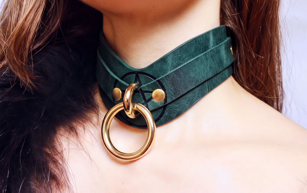 A close-up of a woman's neck wearing a green leather choker necklace with a gold ring.