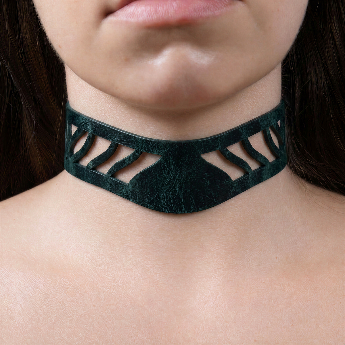 A close-up of a person's neck and chest area wearing a dark green choker necklace with a unique cutout design.
