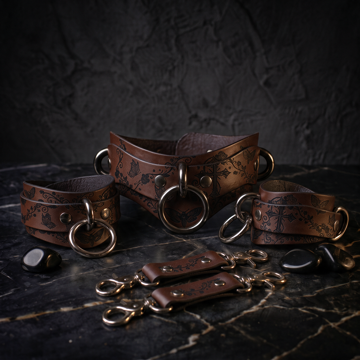 A collection of leather straps and buckles arranged on a dark surface, with some small black stones scattered around.
