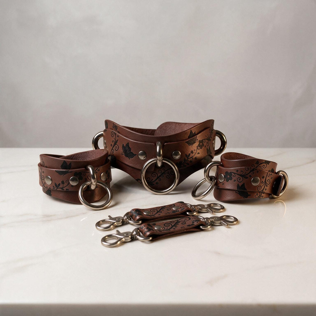 A set of brown leather straps with metal rings and buckles, arranged on a white marble surface.