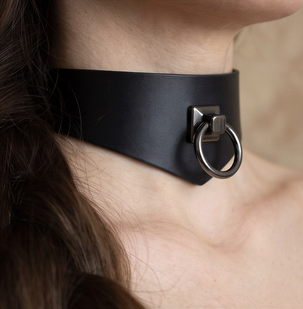 A close-up view of a person's neck and chin area, featuring a black leather choker necklace with a metal ring.