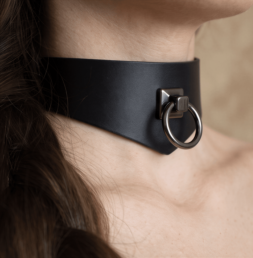 A close-up view of a person's neck and chin area, featuring a black leather choker necklace with a metal ring.