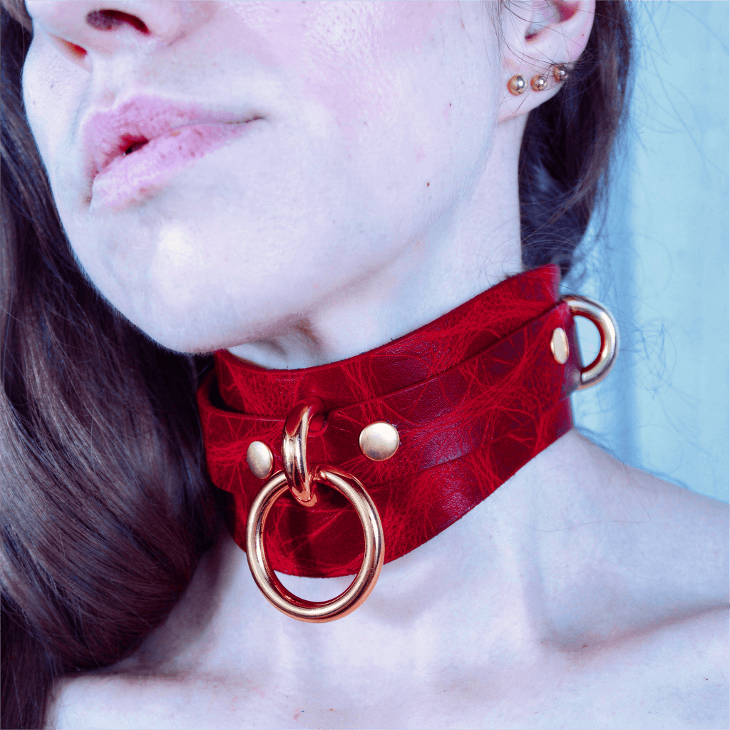A close-up of a person's neck and chest area wearing a red choker necklace with gold-colored metal rings.