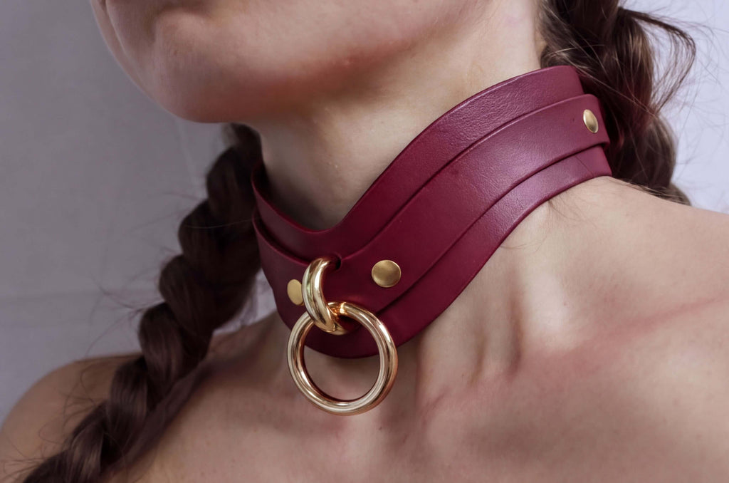 A close-up of a person's neck wearing a burgundy leather choker necklace with a gold ring.