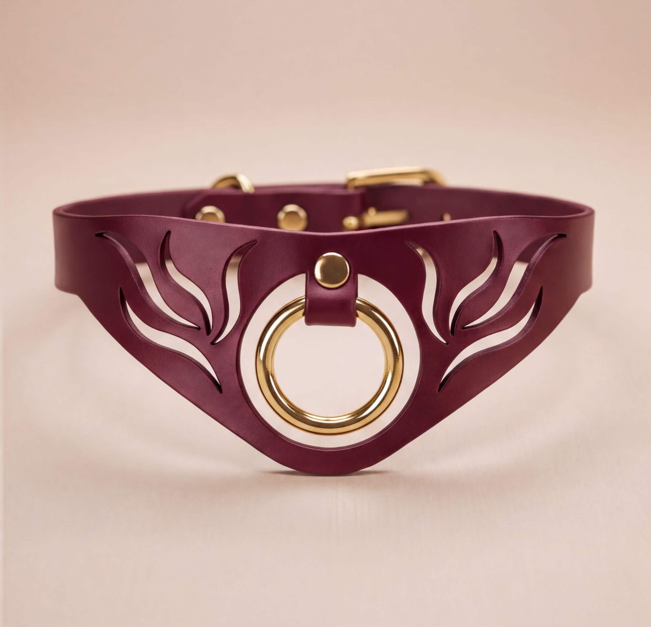 A burgundy leather choker necklace with a gold-colored circular ring and a leaf-like cutout design on the front.