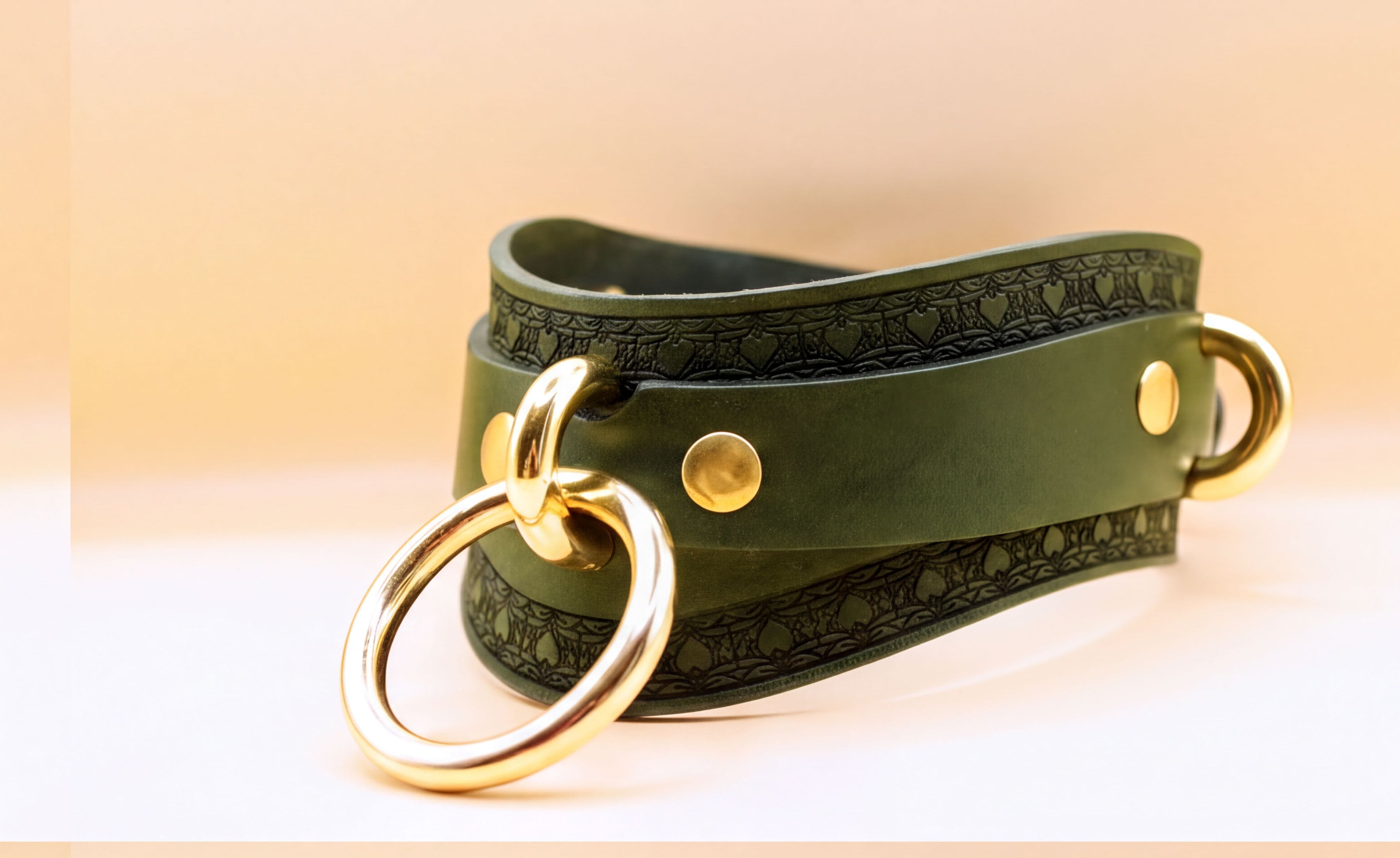 A green leather choker necklace with a gold ring and two gold-colored metal rings on either side.