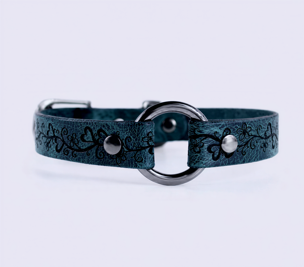 A teal-colored leather collar with a metal ring and decorative floral patterns.