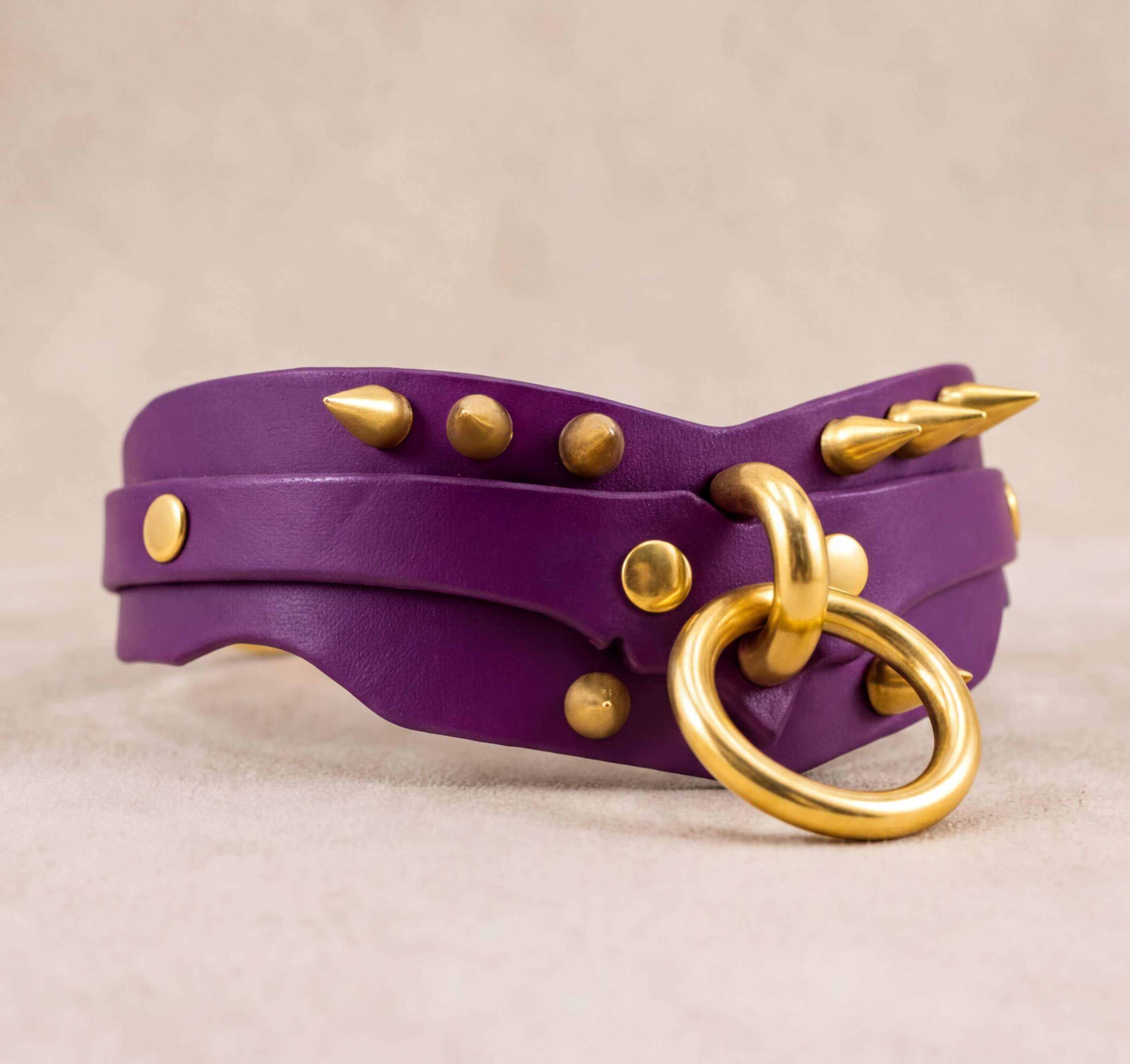 A purple leather choker necklace with gold studs and a gold ring.