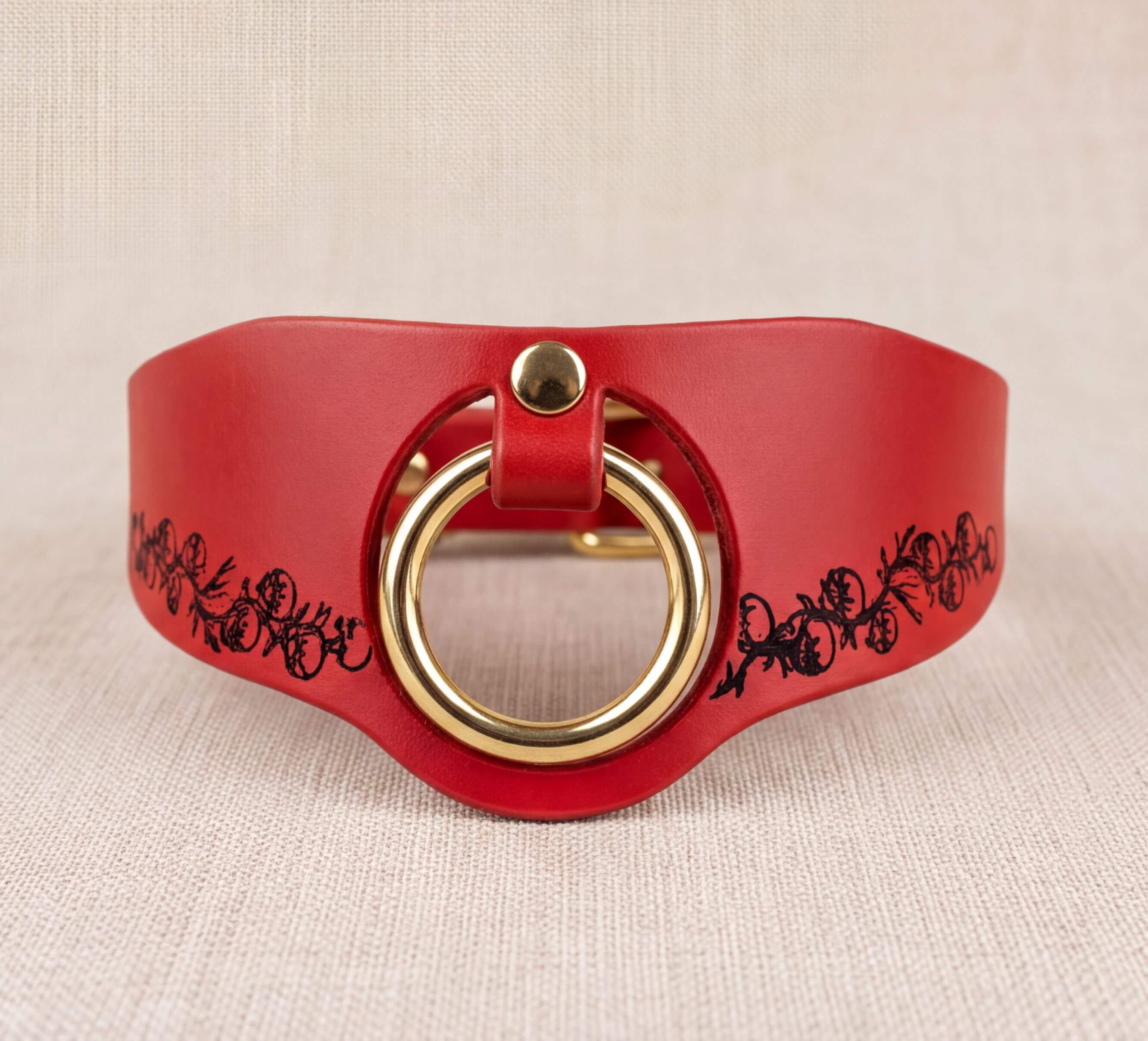 A red leather choker necklace with a gold-colored circular clasp and a floral design on the side.