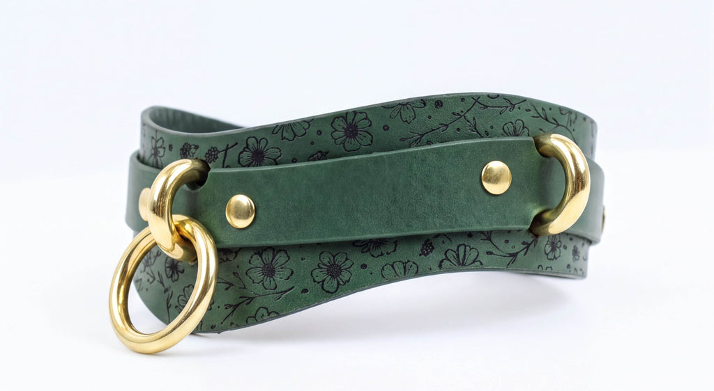 A green leather strap with a floral pattern and two gold-colored metal rings on the ends.