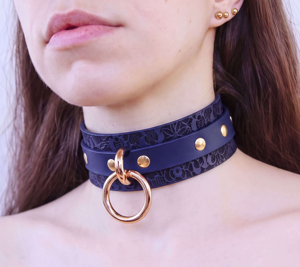 A close-up of a woman's neck and chest area wearing a dark blue choker necklace with a gold ring and studs.