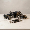 A set of black leather choker necklaces with metal rings and buckles, arranged on a white marble surface.