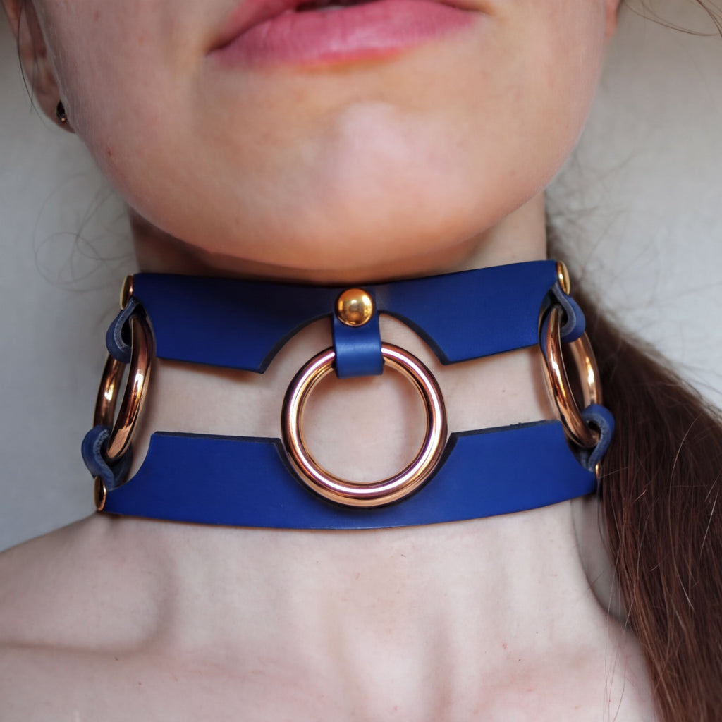 A close-up of a person's neck wearing a blue leather choker necklace with three circular rings.